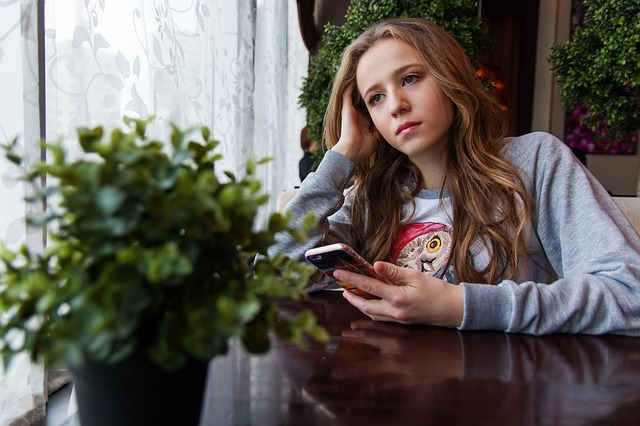 Teenage girl in cafe with smartphone and plant