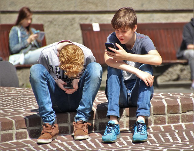 Two boys sitting on steps in sunshine playing with mobile phones