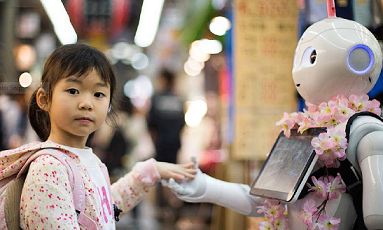 A child holding the hand of Pepper the robot while looking at the camera