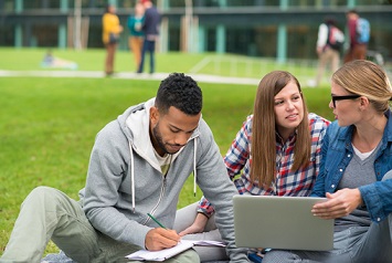 Three students reading on grass
